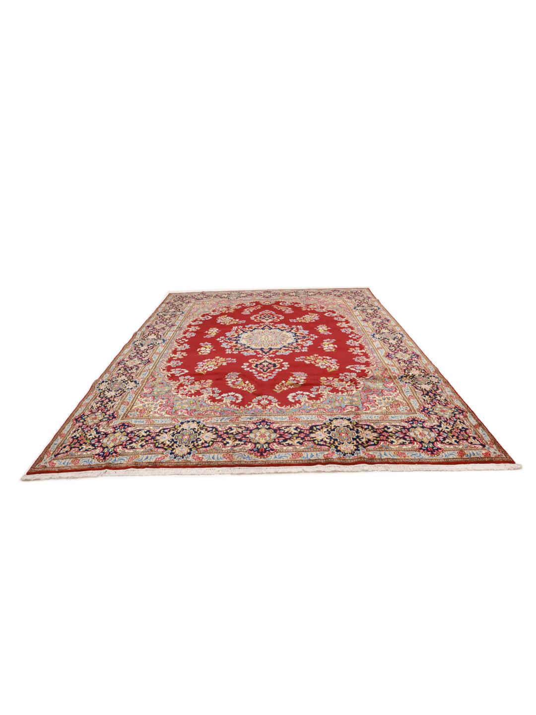 A large rectangular Kerman rug from the Middle East with a deep red field and intricate floral motifs.