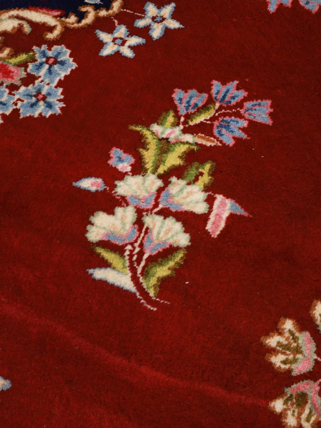 A large rectangular Kerman rug from the Middle East with a deep red field and intricate floral motifs.
