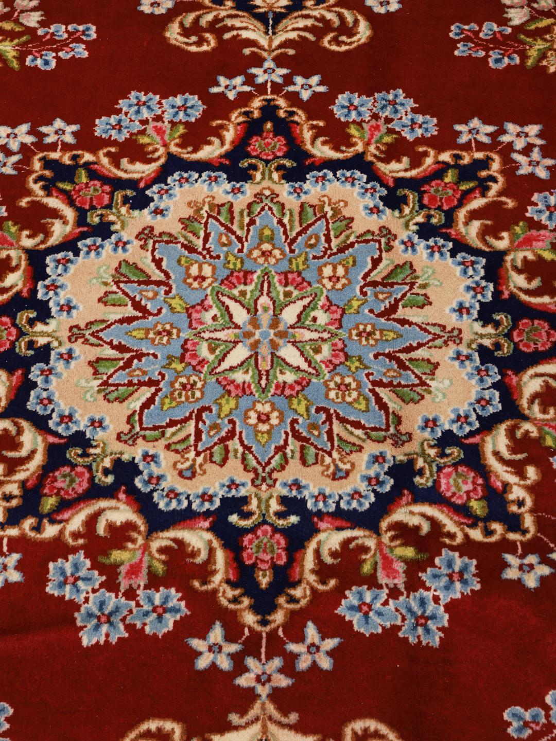 A large rectangular Kerman rug from the Middle East with a deep red field and intricate floral motifs.