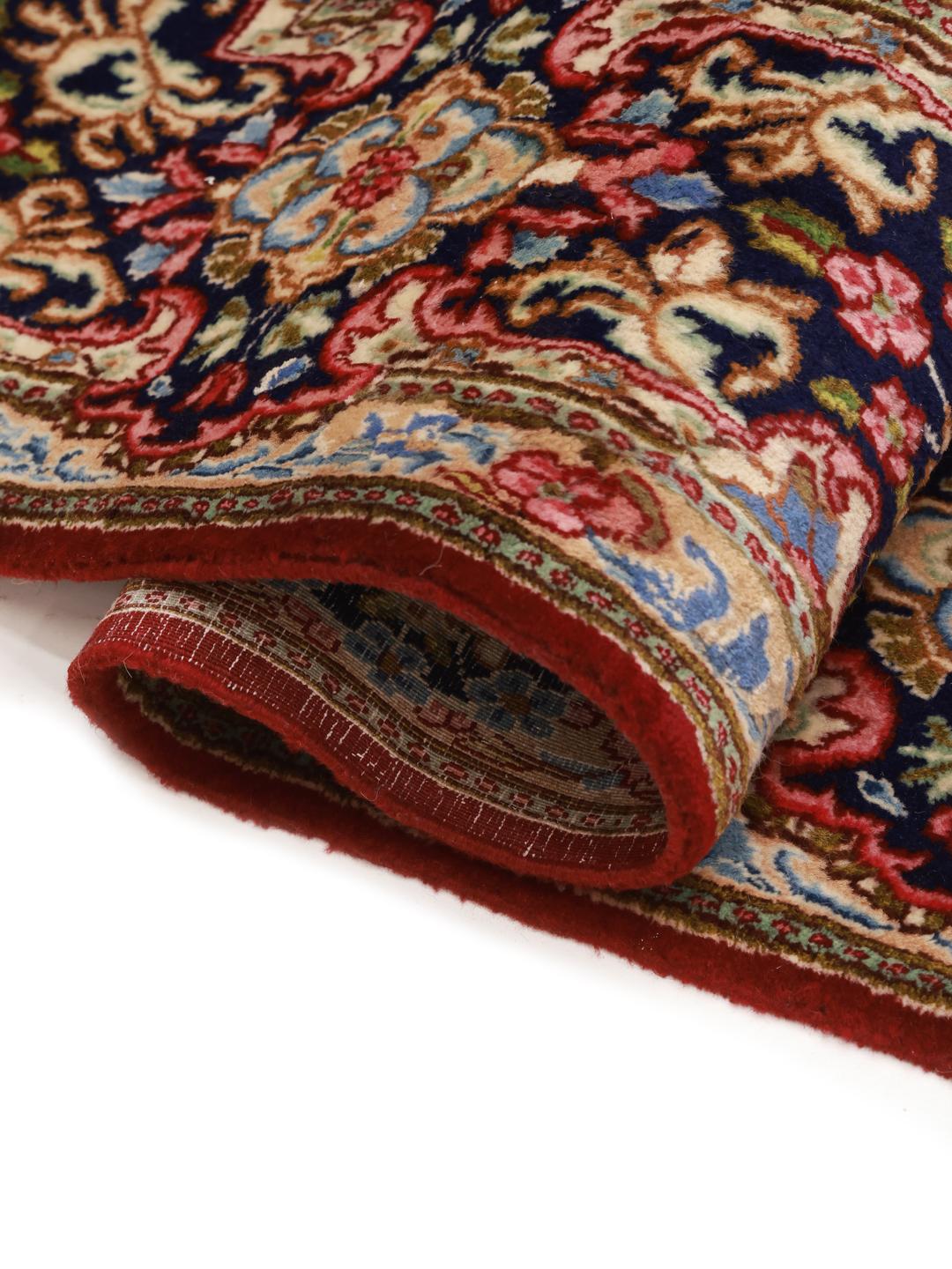 A large rectangular Kerman rug from the Middle East with a deep red field and intricate floral motifs.