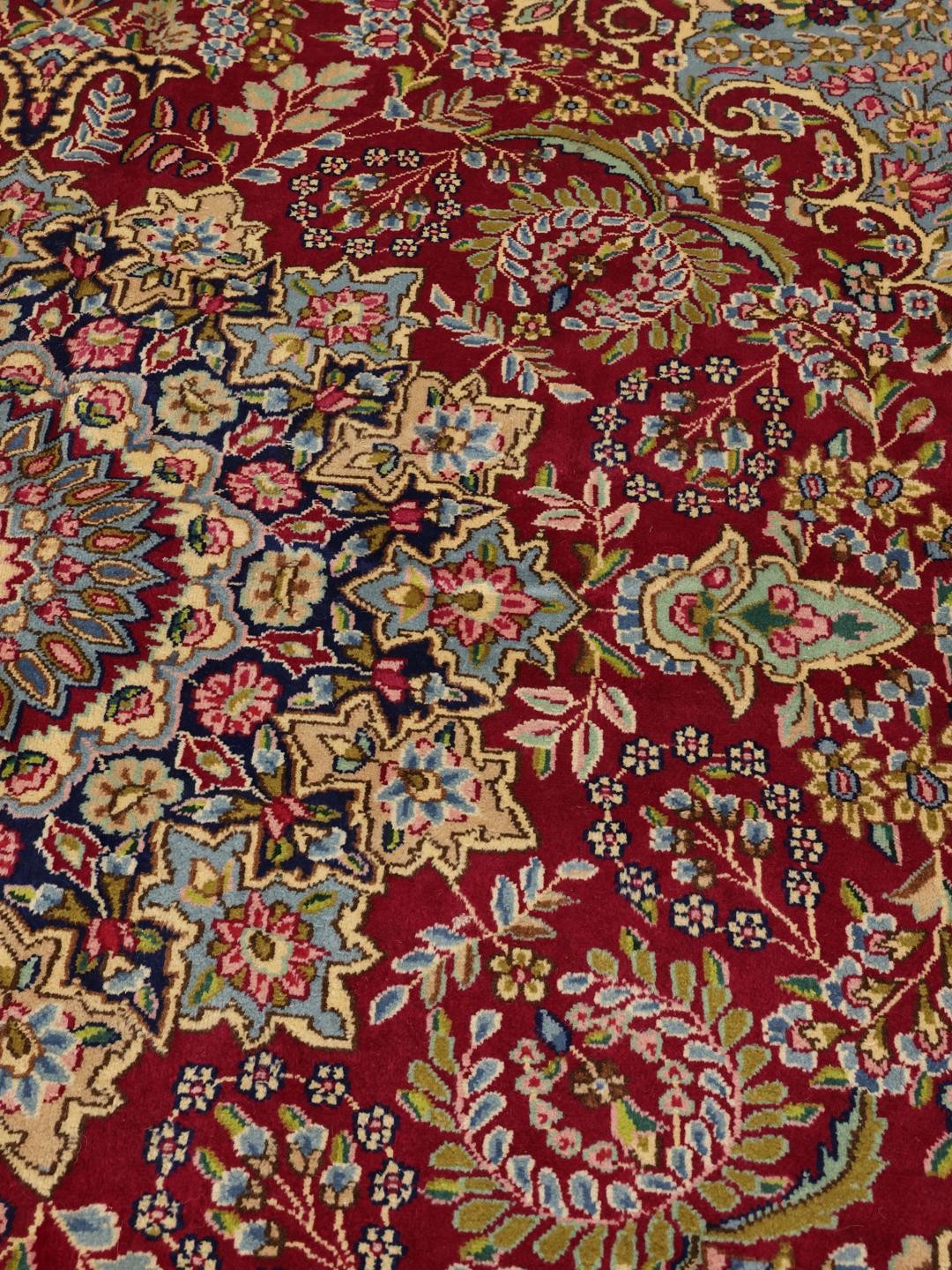 Een groot rechthoekig Kerman-tapijt uit het Midden-Oosten met een levendig rood en blauw bloemenpatroon.