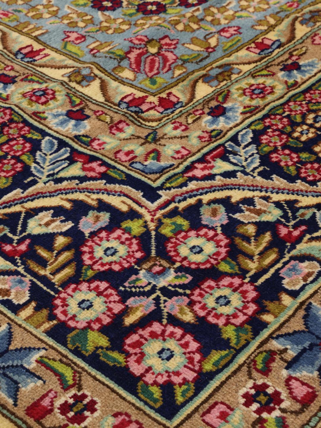 Een groot rechthoekig Kerman-tapijt uit het Midden-Oosten met een levendig rood en blauw bloemenpatroon.