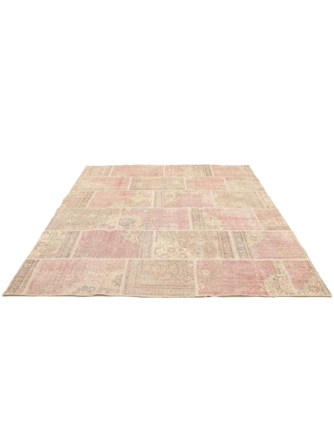 Et kvadratisk patchwork-tæppe med lyserøde og beige blomstermotiver og en patineret finish.