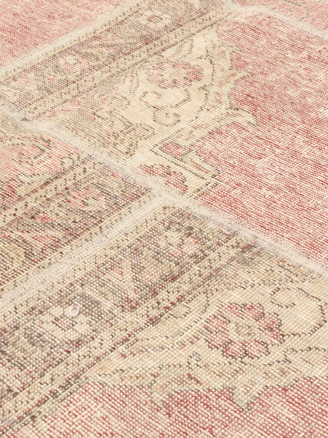Et kvadratisk patchwork-tæppe med lyserøde og beige blomstermotiver og en patineret finish.