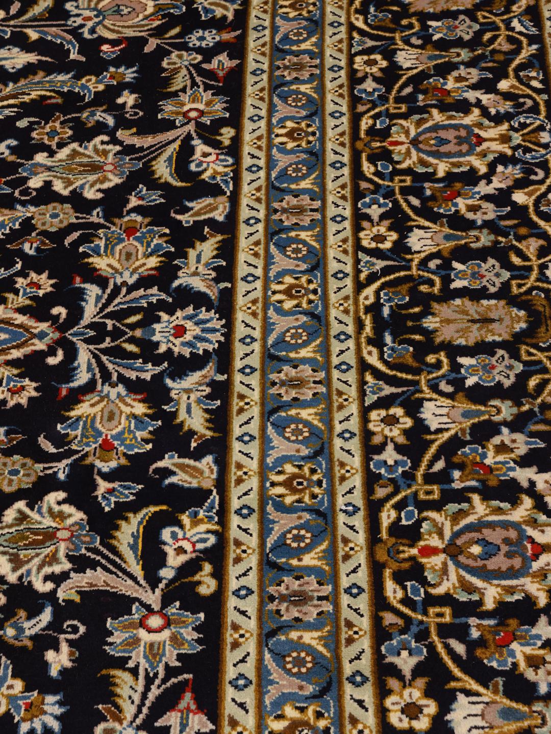 A large, rectangular hand-knotted Keshan rug from the Middle East featuring a floral pattern in dark-blue and cream tones.
