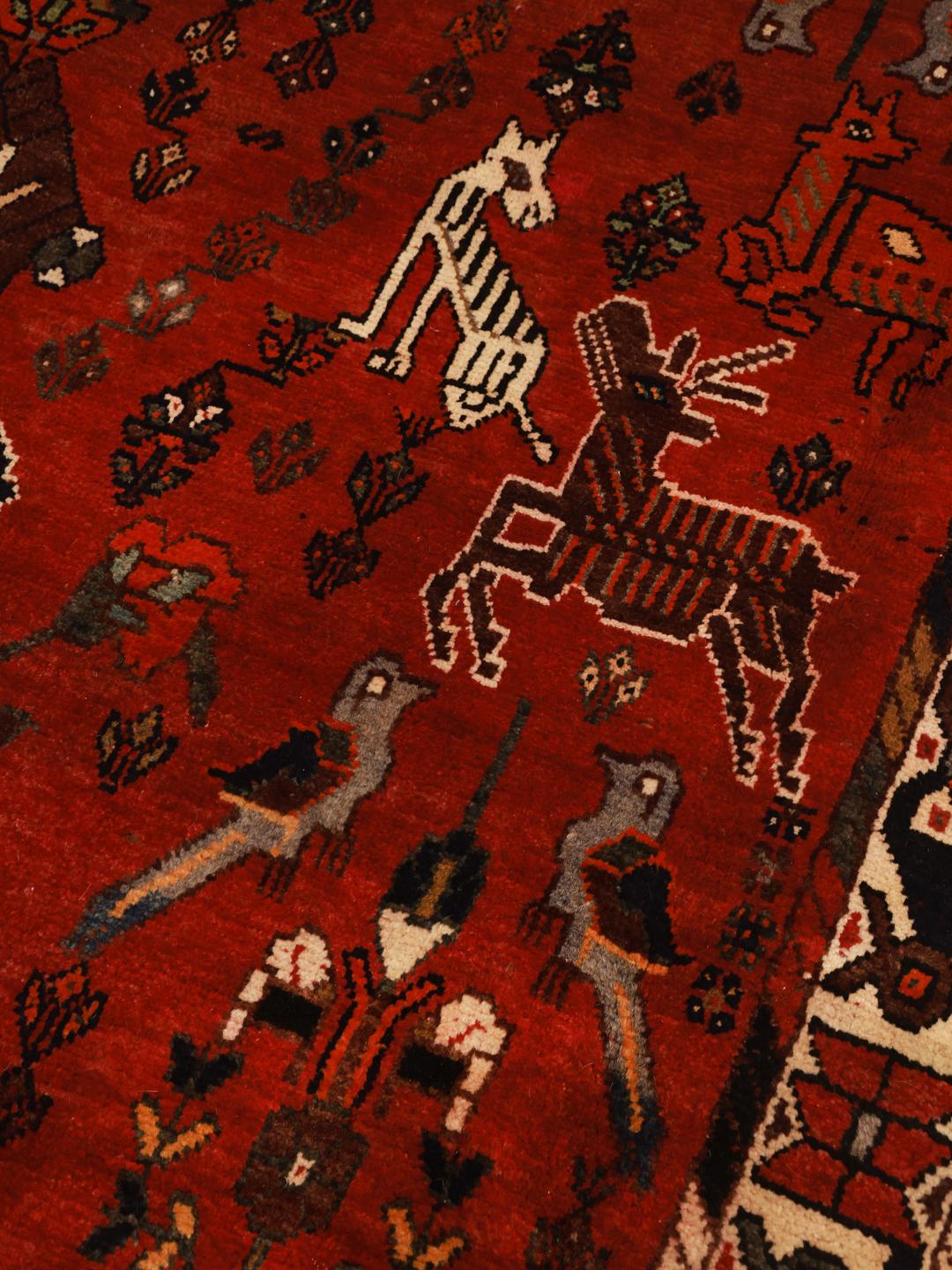 A unique hand-knotted Ghashghai rug from the Middle East with a vibrant red field and animal motifs.