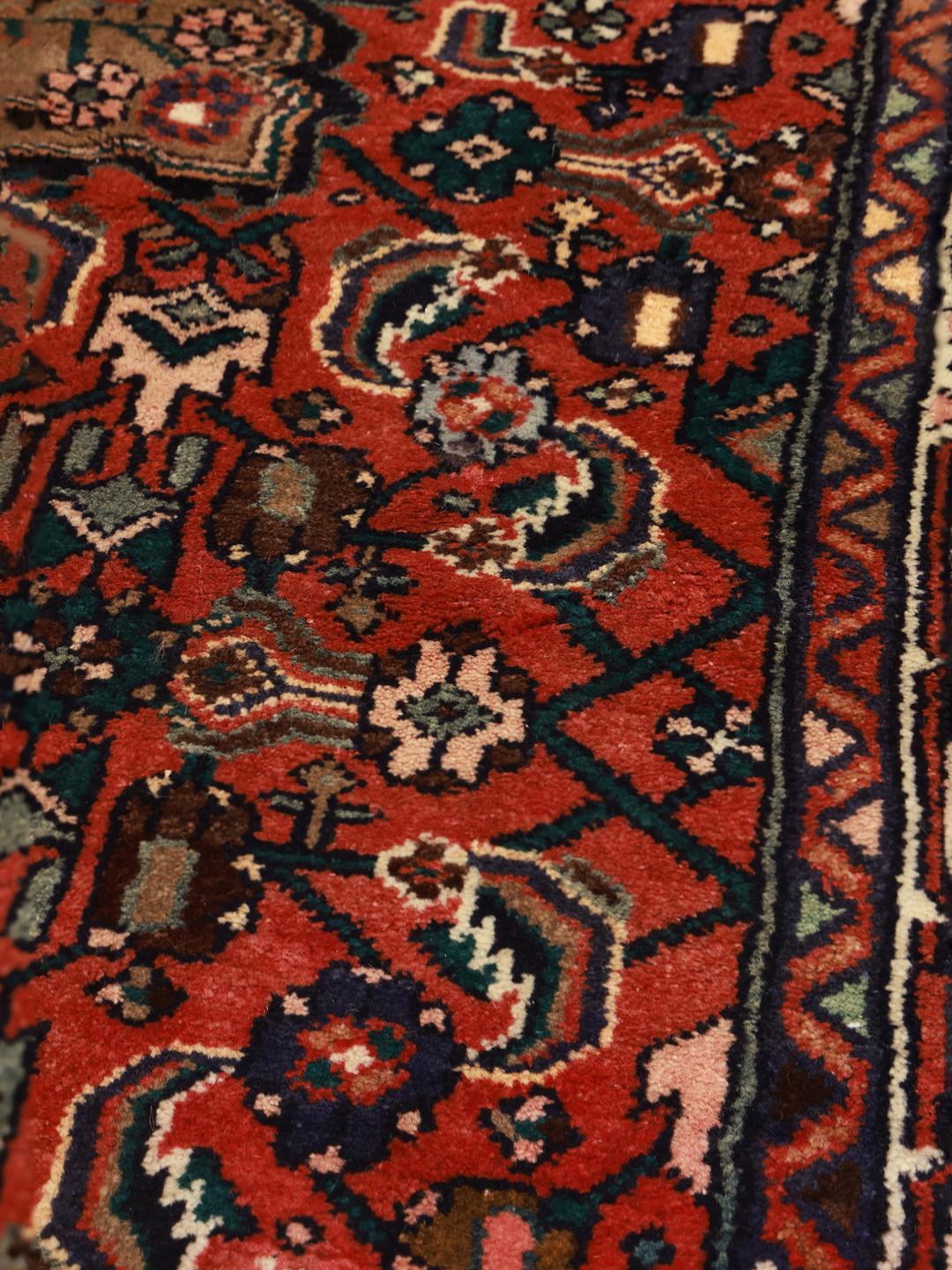 Een handgeknoopt Hosseinabad tapijt uit het Midden-Oosten met een rood veld en traditionele geometrische motieven.