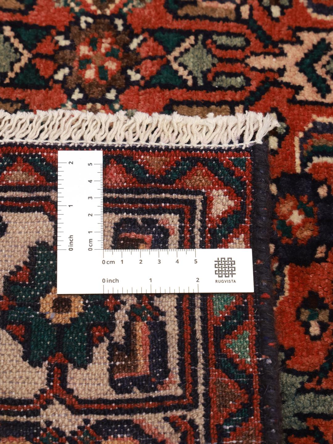 Een handgeknoopt Hosseinabad tapijt uit het Midden-Oosten met een rood veld en traditionele geometrische motieven.