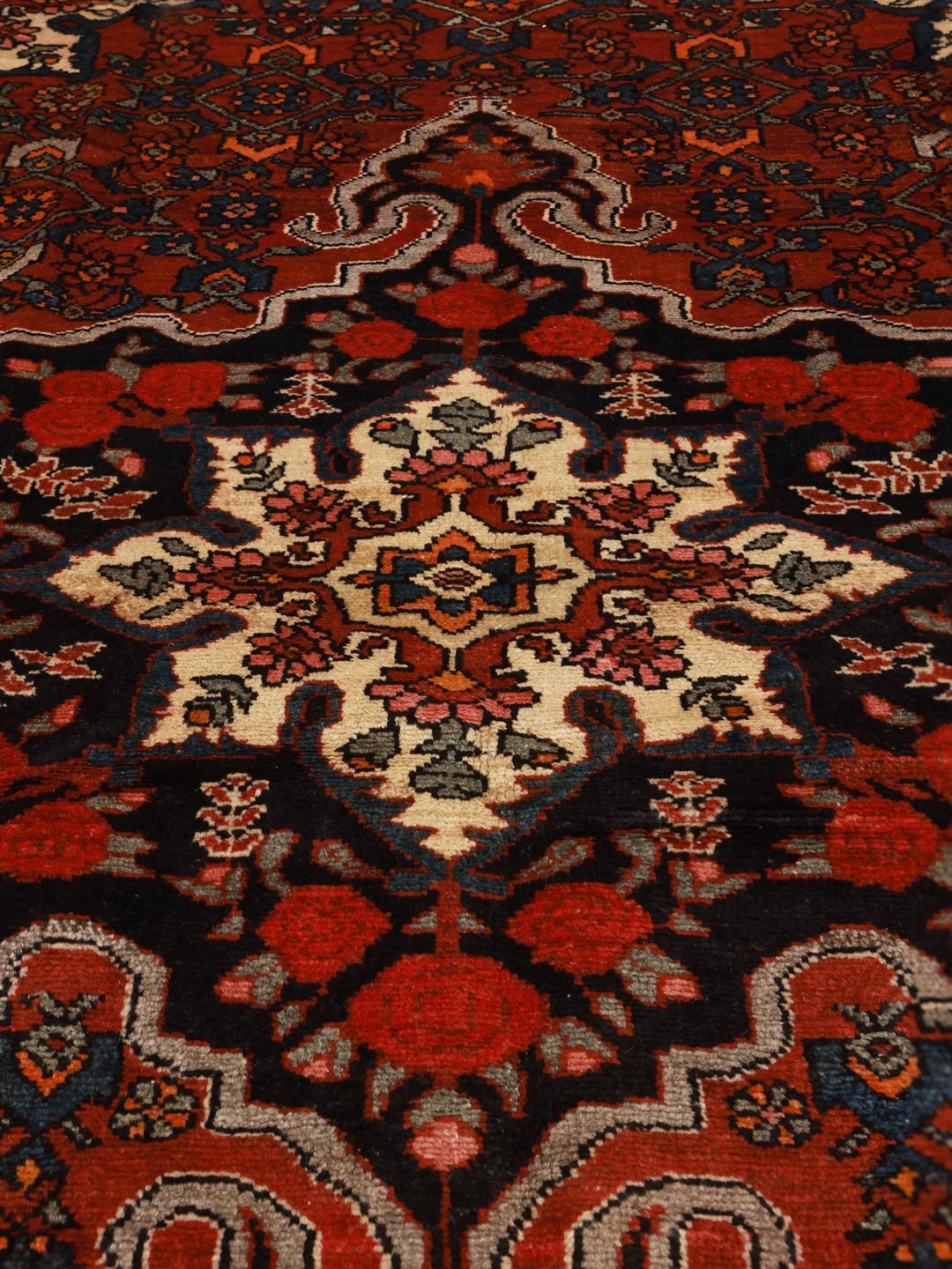 A hand-knotted Hosseinabad wool rug from the Middle East featuring a red field and central medallion.
