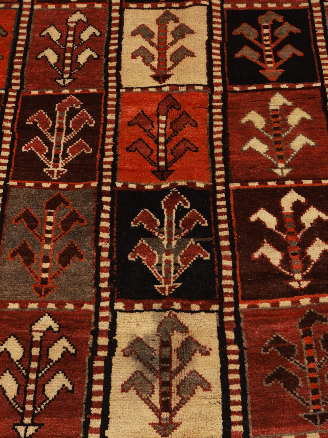 A hand-knotted Qashqai rug from the Middle East featuring a vibrant red field with geometric floral motifs.