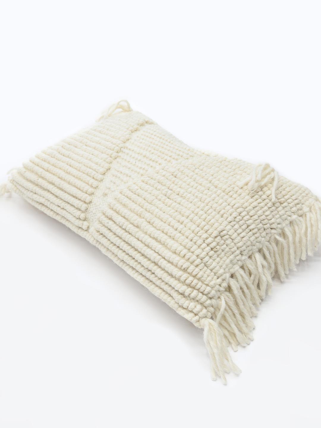 Witte kussenhoes met een handgeweven wollen textuur en franjes.