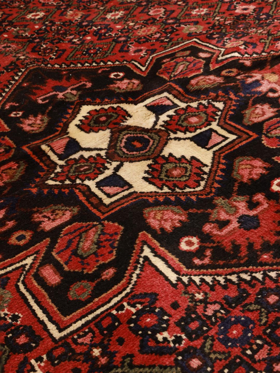 A hand-knotted Hosseinabad rug from the Middle East in deep red and dark blue tones.
