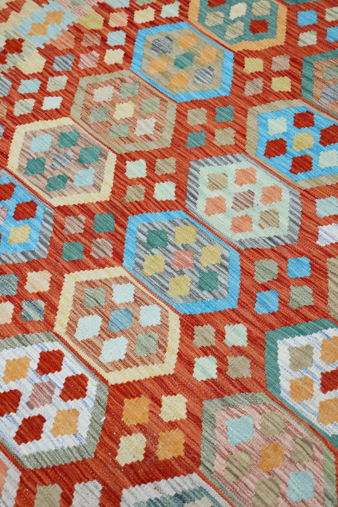 Een groot rechthoekig handgeweven Afghaans kelim tapijt met een levendig rood veld en geometrische zeshoekige patronen.