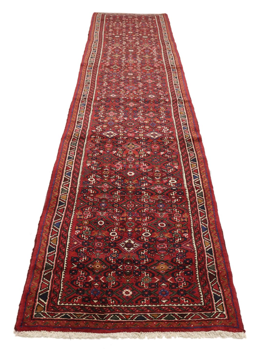 Un long tapis couloir Hosseinabad noué à la main en provenance du Moyen-Orient dans des tons rouge foncé.