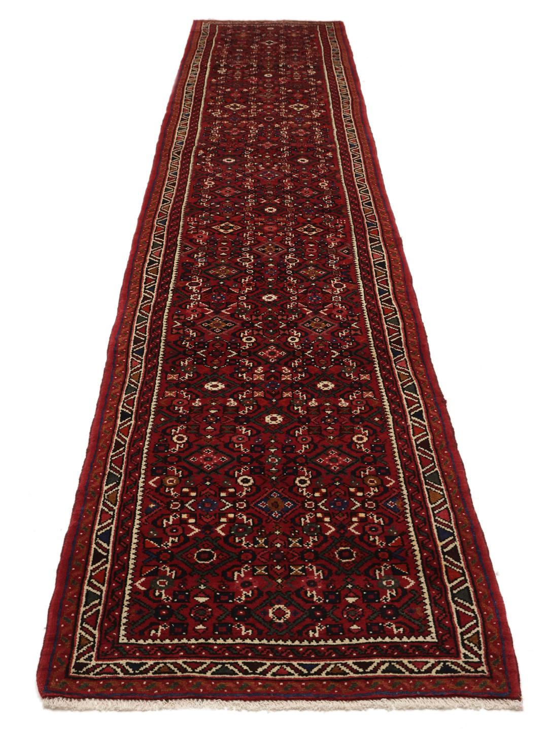 Un long tapis couloir Hosseinabad noué à la main en provenance du Moyen-Orient dans des tons rouge foncé.