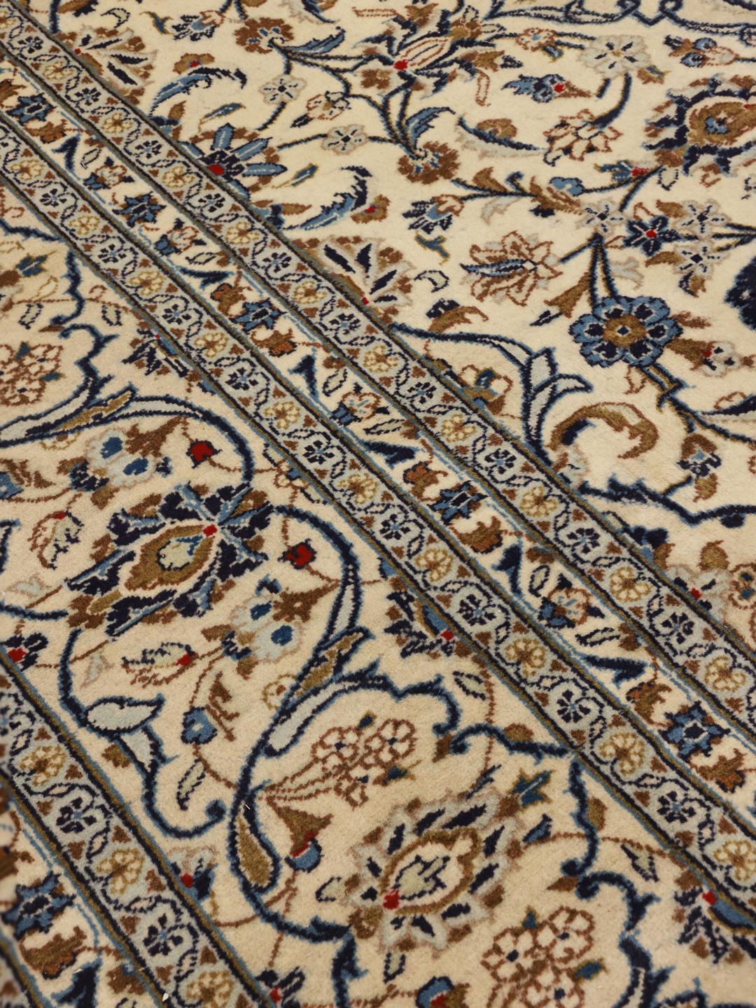 A rectangular Keshan rug from the Middle East featuring beige, blue, and brown floral patterns.