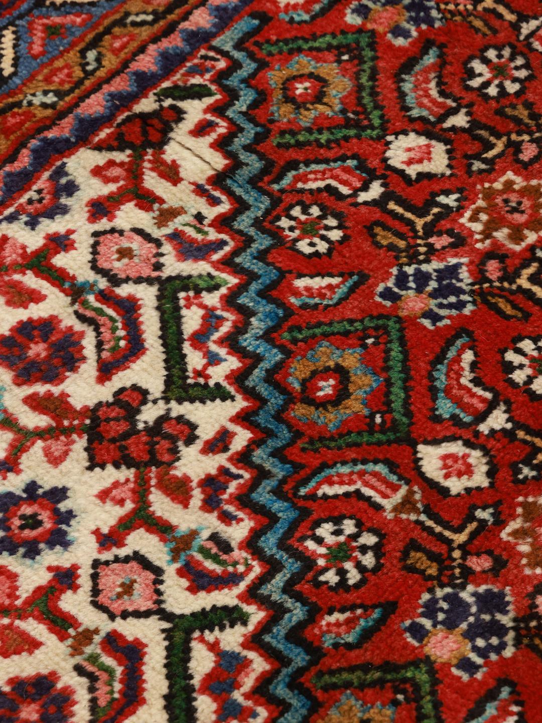 Hand-knotted Hosseinabad rug from the Middle East with a red field and decorative borders.