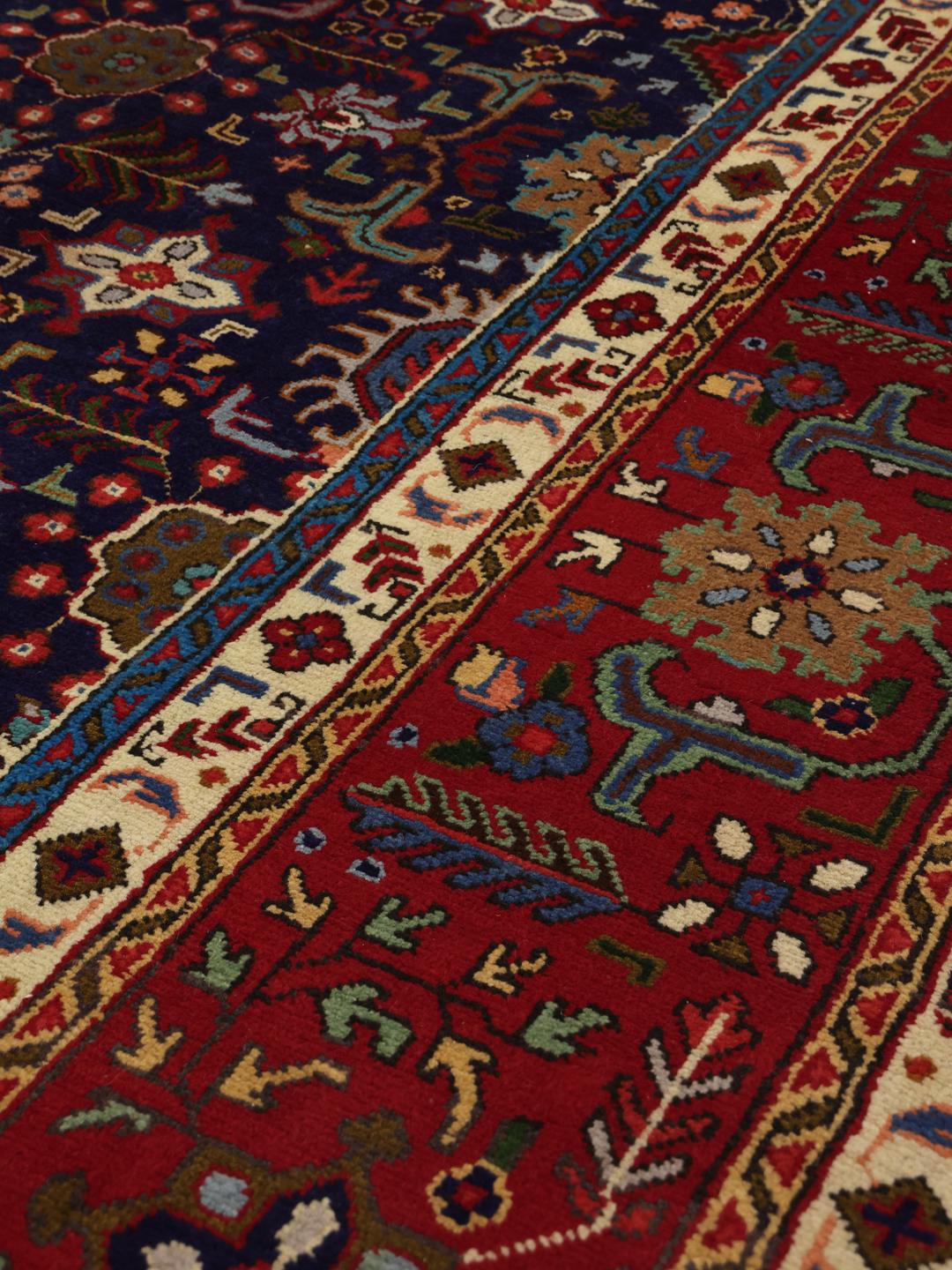 A large rectangular Tabriz rug from the Middle East featuring a dark-blue field and dark-red borders.