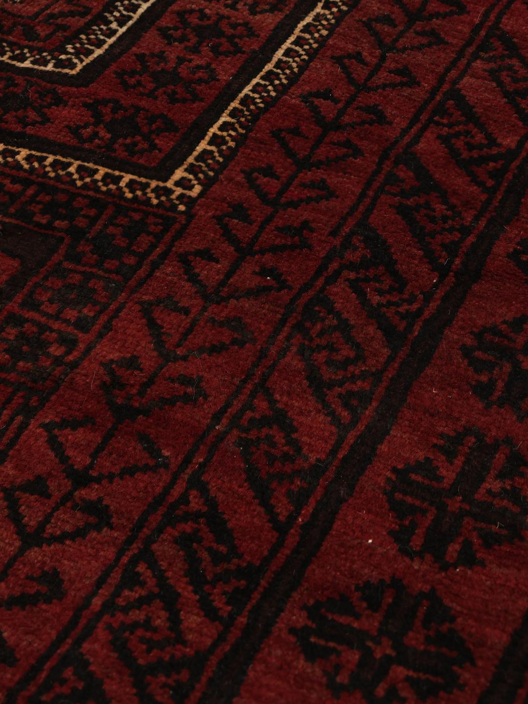 A hand-knotted Middle Eastern Beluch rug in deep red and black tones with geometric patterns.