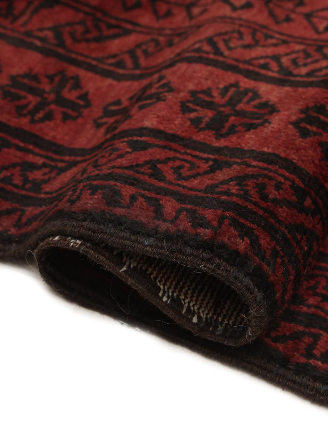 A hand-knotted Middle Eastern Beluch rug in deep red and black tones with geometric patterns.
