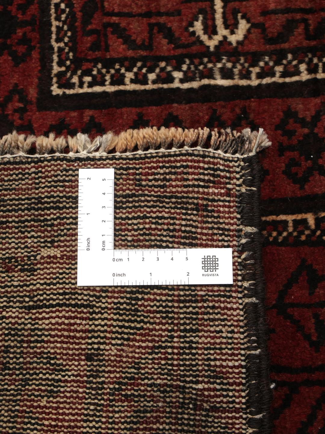 A hand-knotted Middle Eastern Beluch rug in deep red and black tones with geometric patterns.