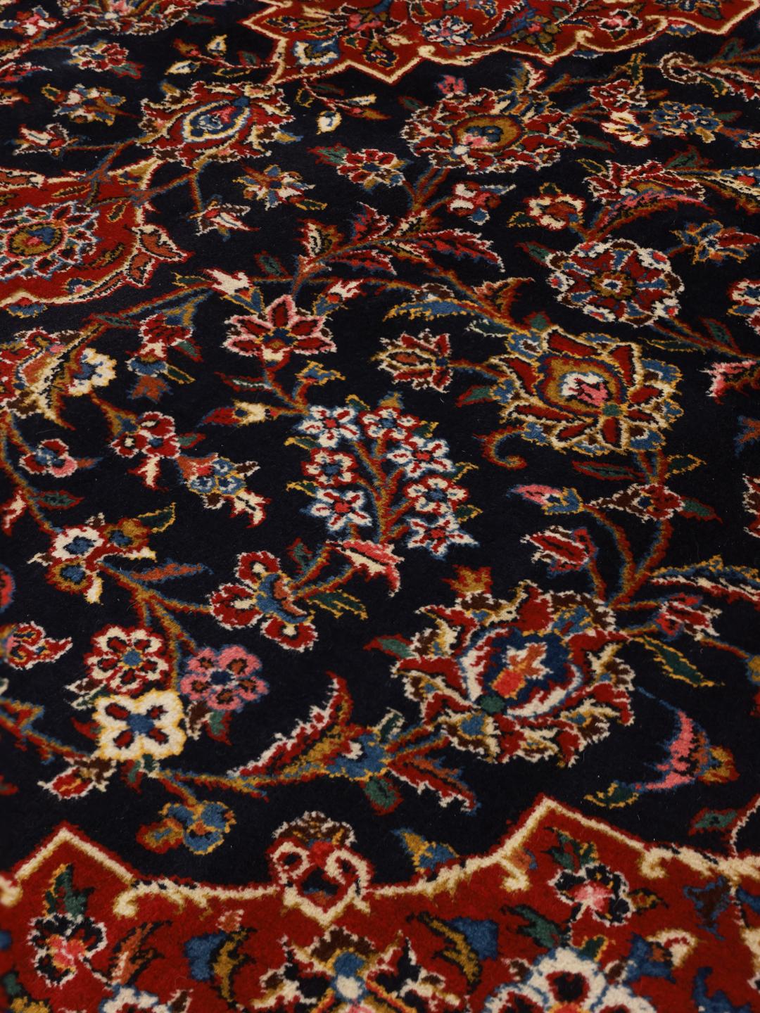 A large rectangular hand-knotted Keshan rug from the Middle East with a dark-blue and dark-red floral pattern.