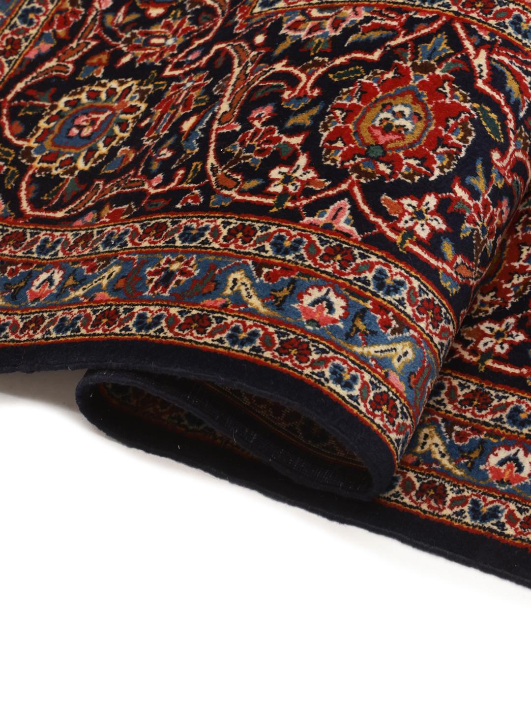 A large rectangular hand-knotted Keshan rug from the Middle East with a dark-blue and dark-red floral pattern.