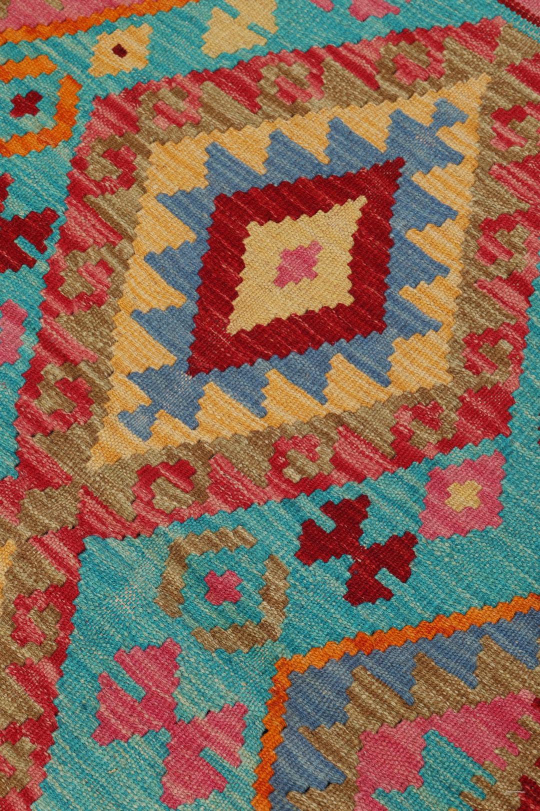 Håndvævet afghansk Kelim-tæppe med geometriske mønstre i rød, blå og pink.