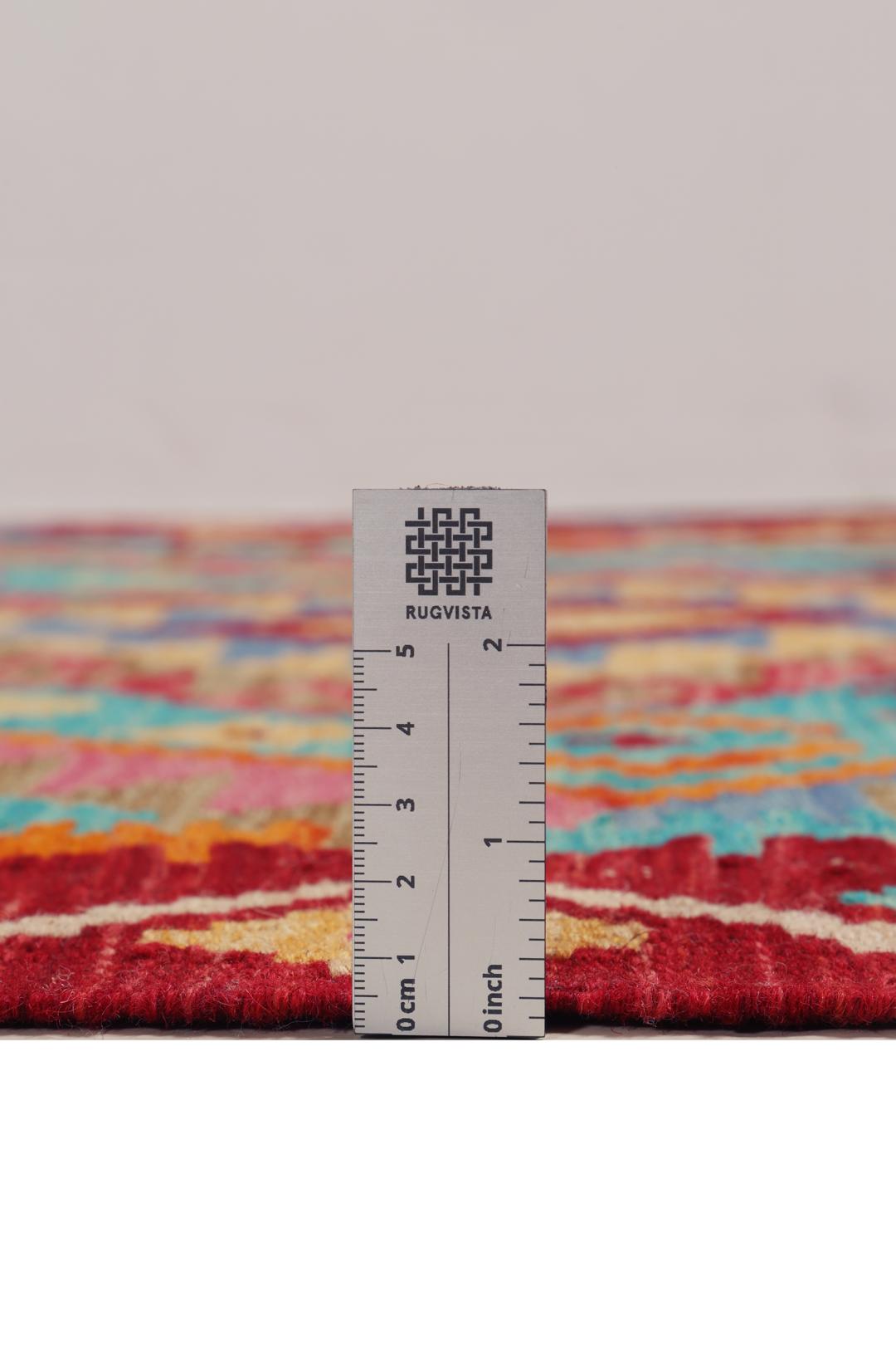 Håndvævet afghansk Kelim-tæppe med geometriske mønstre i rød, blå og pink.