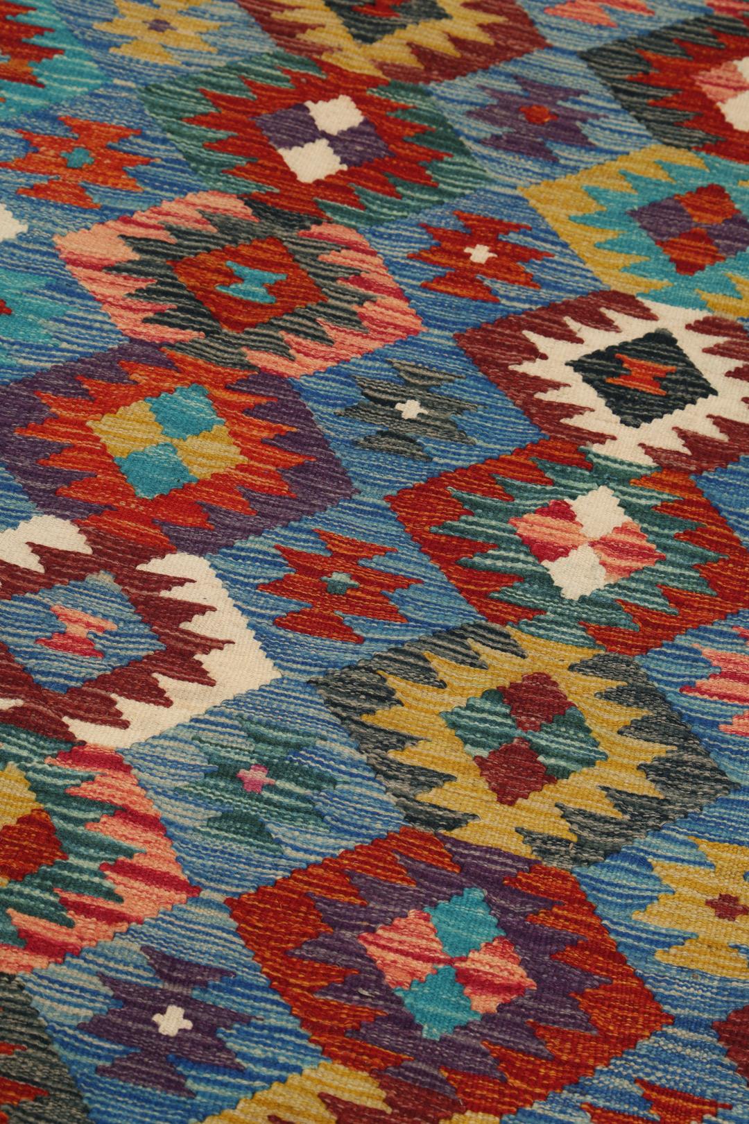 Een groot rechthoekig handgeweven Kelim-tapijt uit Afghanistan met een levendig, veelkleurig geometrisch patroon.