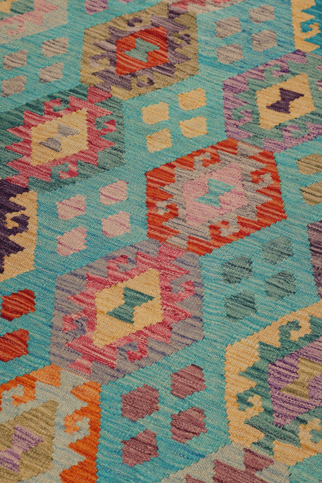 Et håndvævet, unikt afghansk Kelim tæppe med en levende blågrøn bund og farverige geometriske diamantmønstre.