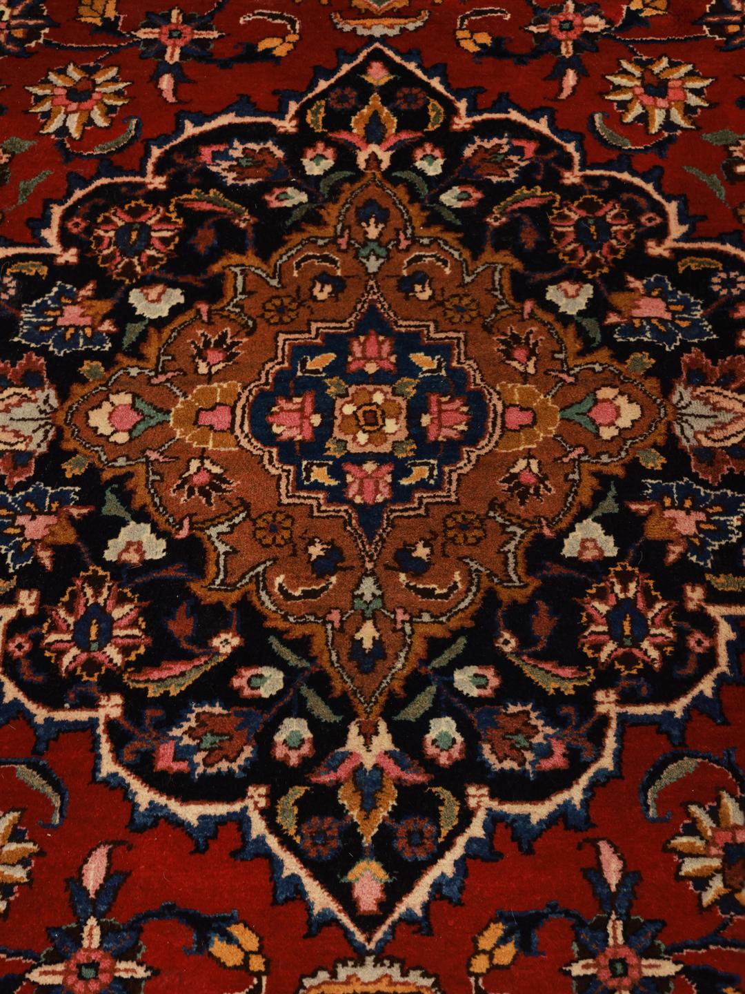 Een handgeknoopt Mashad-tapijt met een rood veld en verfijnde bloemmotieven in het medaillon.