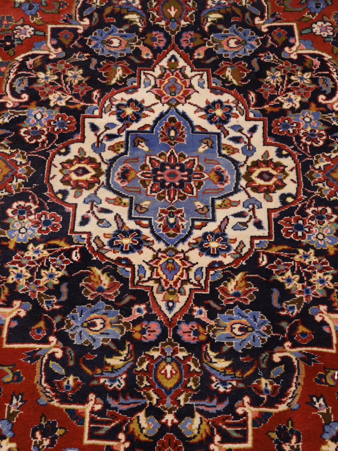 Een groot rechthoekig handgeknoopt Keshan-tapijt uit het Midden-Oosten met een rood veld en een ingewikkeld blauw en wit bloemenmedaillon.