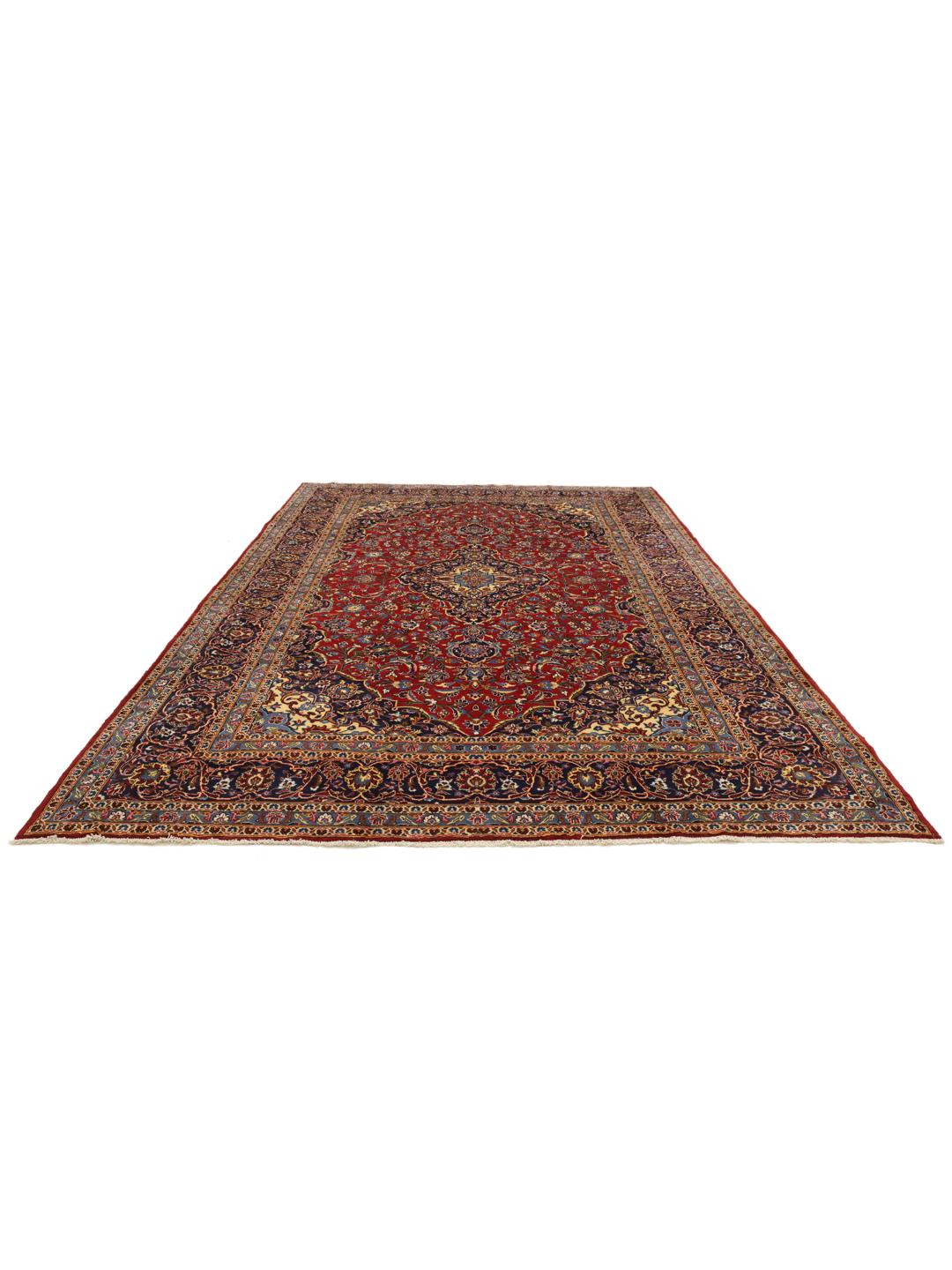 A large rectangular Keshan rug from the Middle East with a rich red floral field and blue accents.