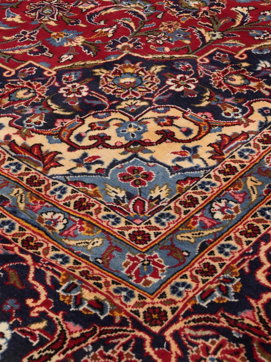 A large rectangular Keshan rug from the Middle East with a rich red floral field and blue accents.
