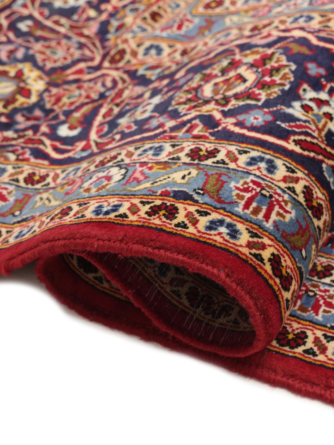 A large rectangular Keshan rug from the Middle East with a rich red floral field and blue accents.