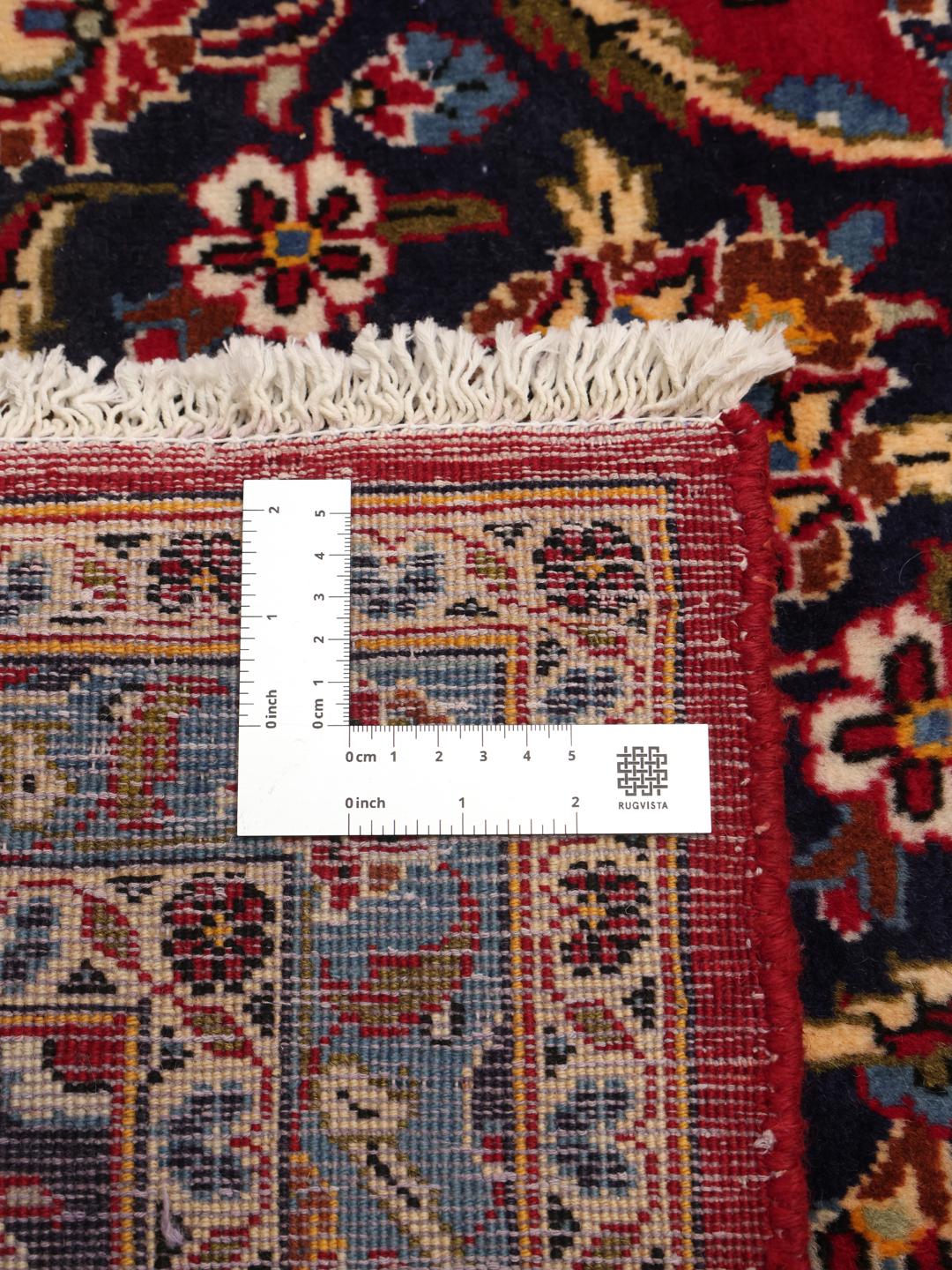 A large rectangular Keshan rug from the Middle East with a rich red floral field and blue accents.
