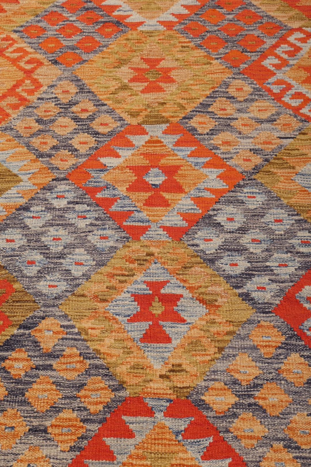 A rectangular Afghan Kelim rug featuring a vibrant geometric pattern in shades of orange, grey, and ochre.