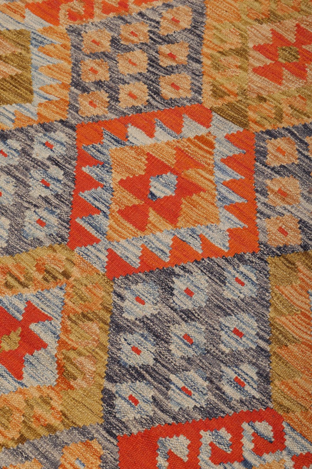 A rectangular Afghan Kelim rug featuring a vibrant geometric pattern in shades of orange, grey, and ochre.