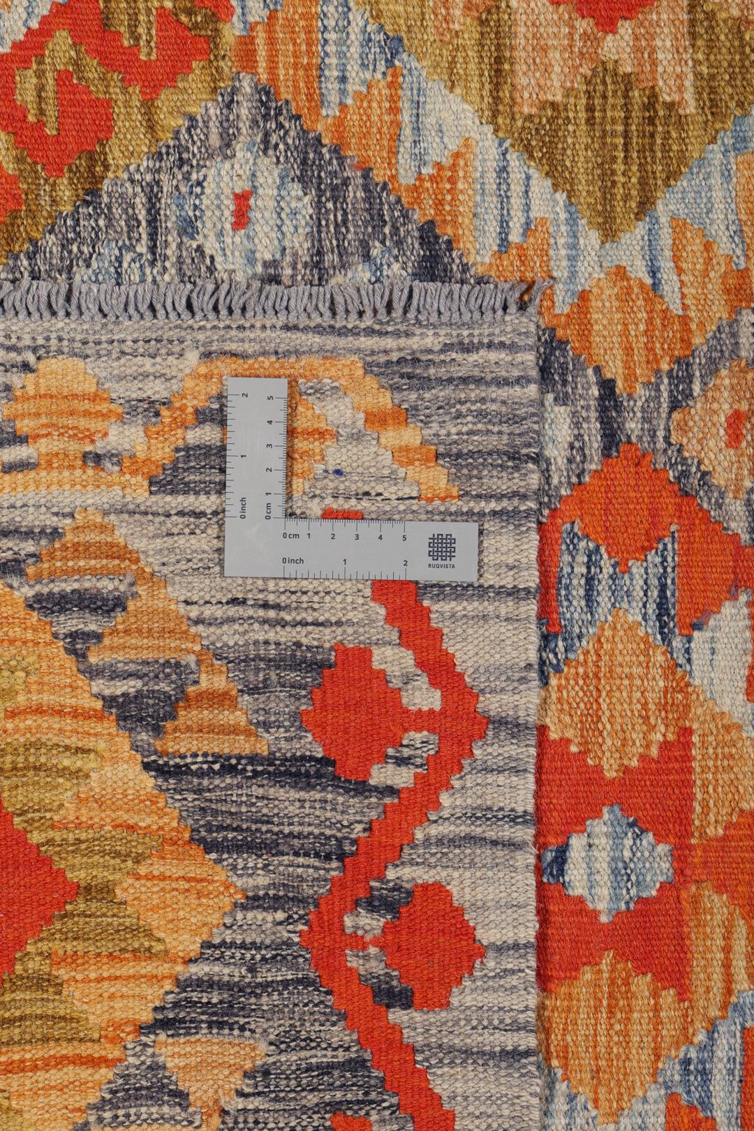 A rectangular Afghan Kelim rug featuring a vibrant geometric pattern in shades of orange, grey, and ochre.