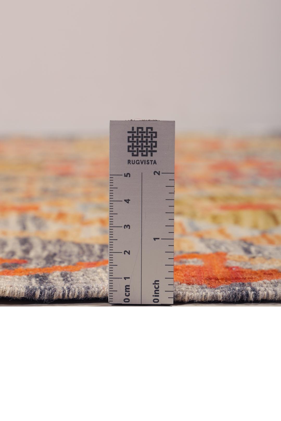 A rectangular Afghan Kelim rug featuring a vibrant geometric pattern in shades of orange, grey, and ochre.