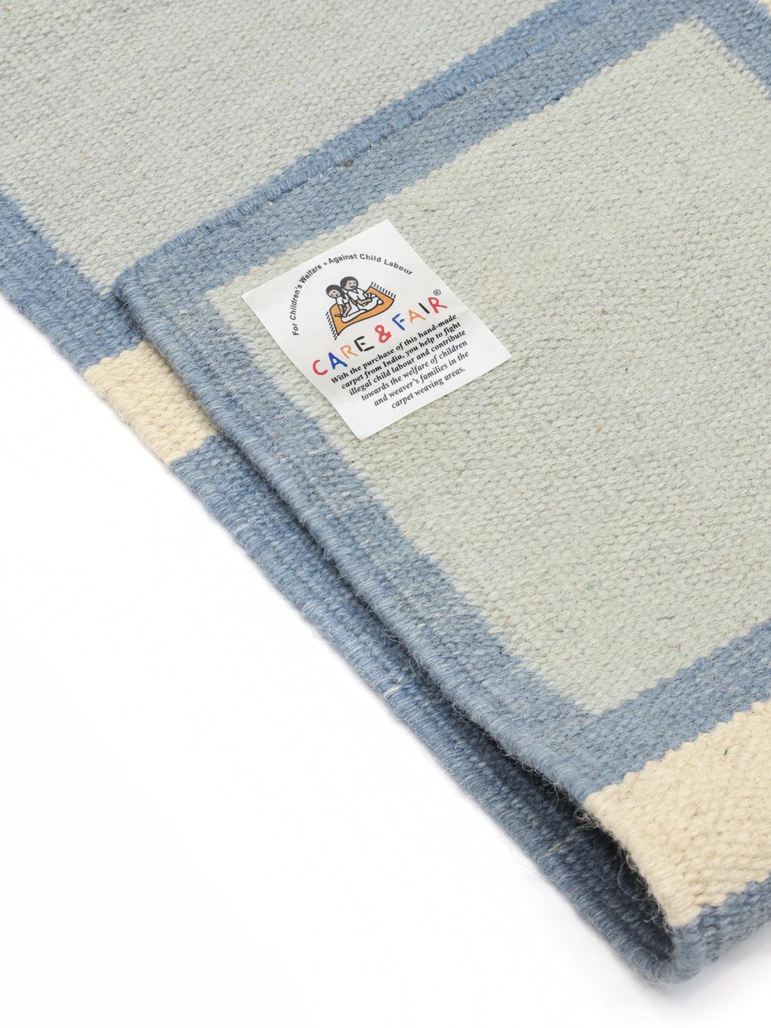 Et rektangulært uldtæppe med et geometrisk gittermønster i blå, beige og hvide nuancer.