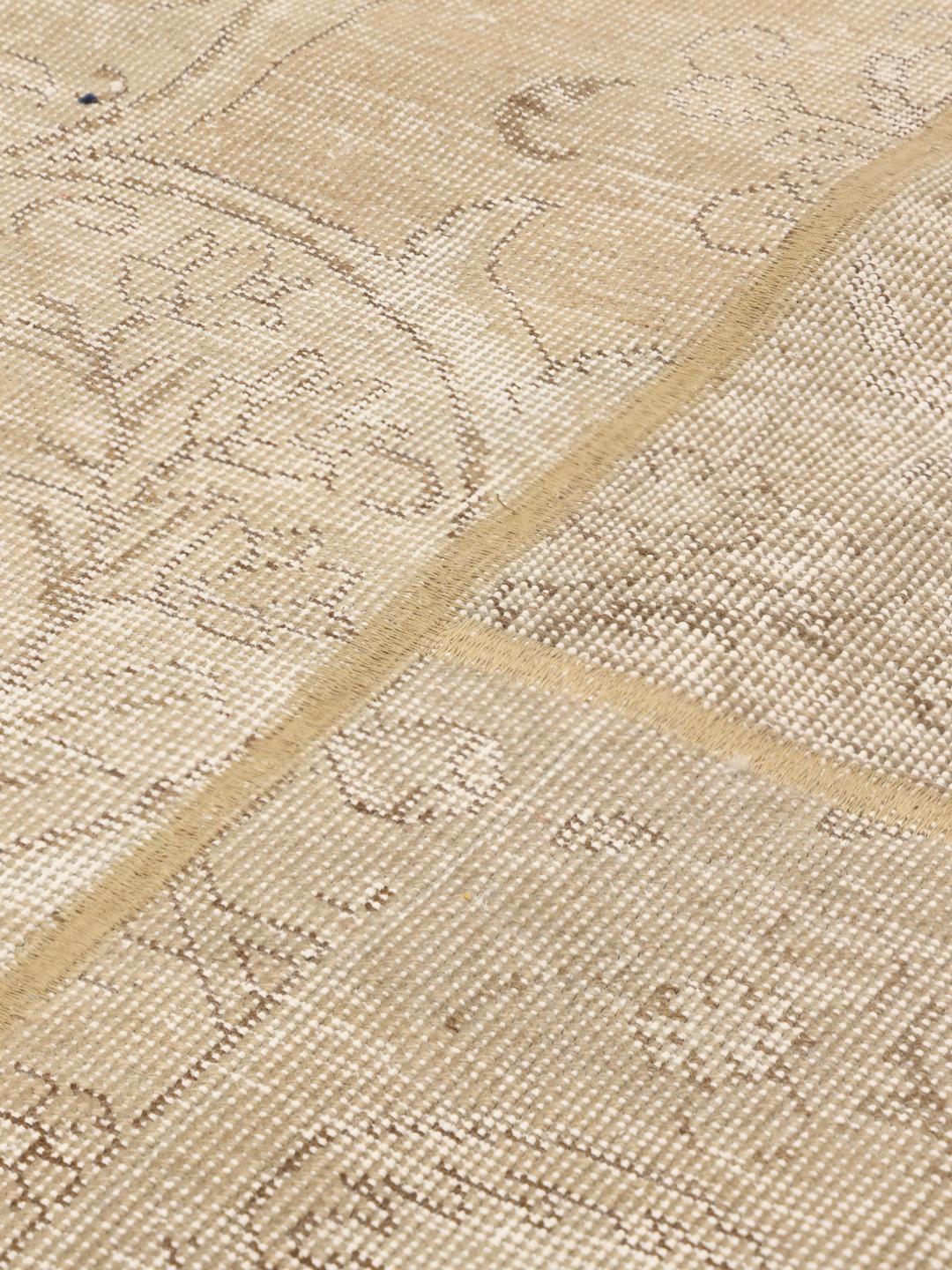 Et rundt beige patchworktæppe med dekorative mønstre og en slidt, vintage-inspireret finish.