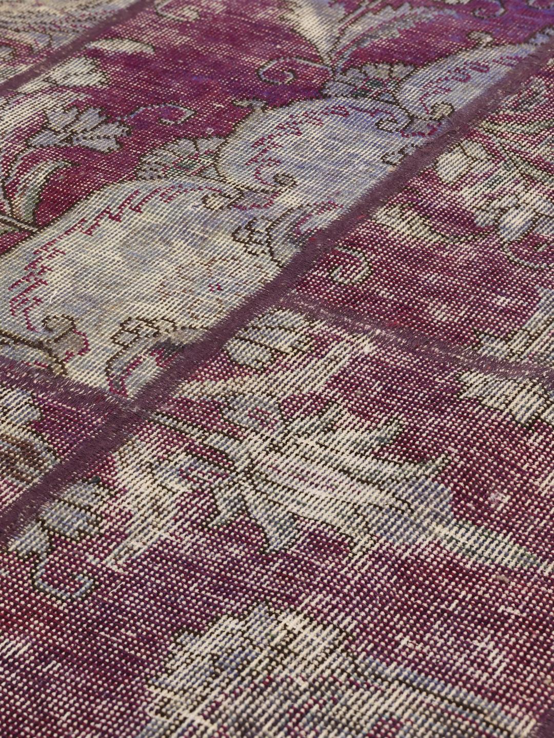 Rundt patchwork-tæppe med udsmykkede blomstermønstre i mørkerøde og grå nuancer