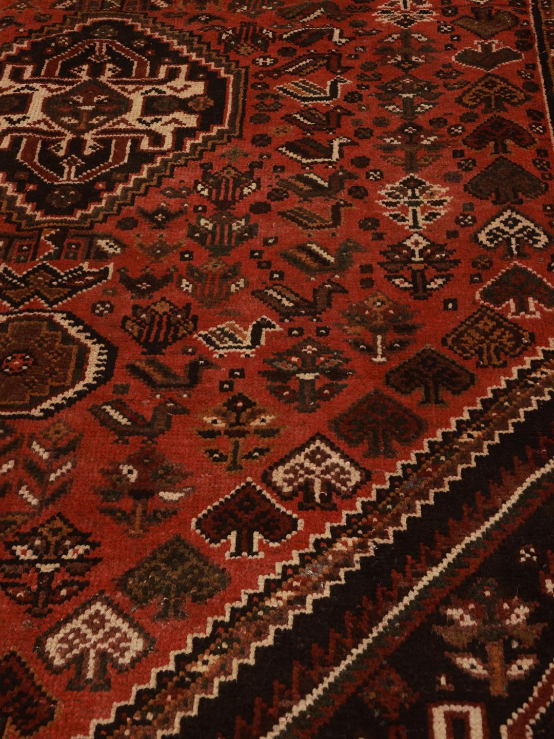 A hand-knotted Qashqai rug from the Middle East featuring a red field and decorative borders.