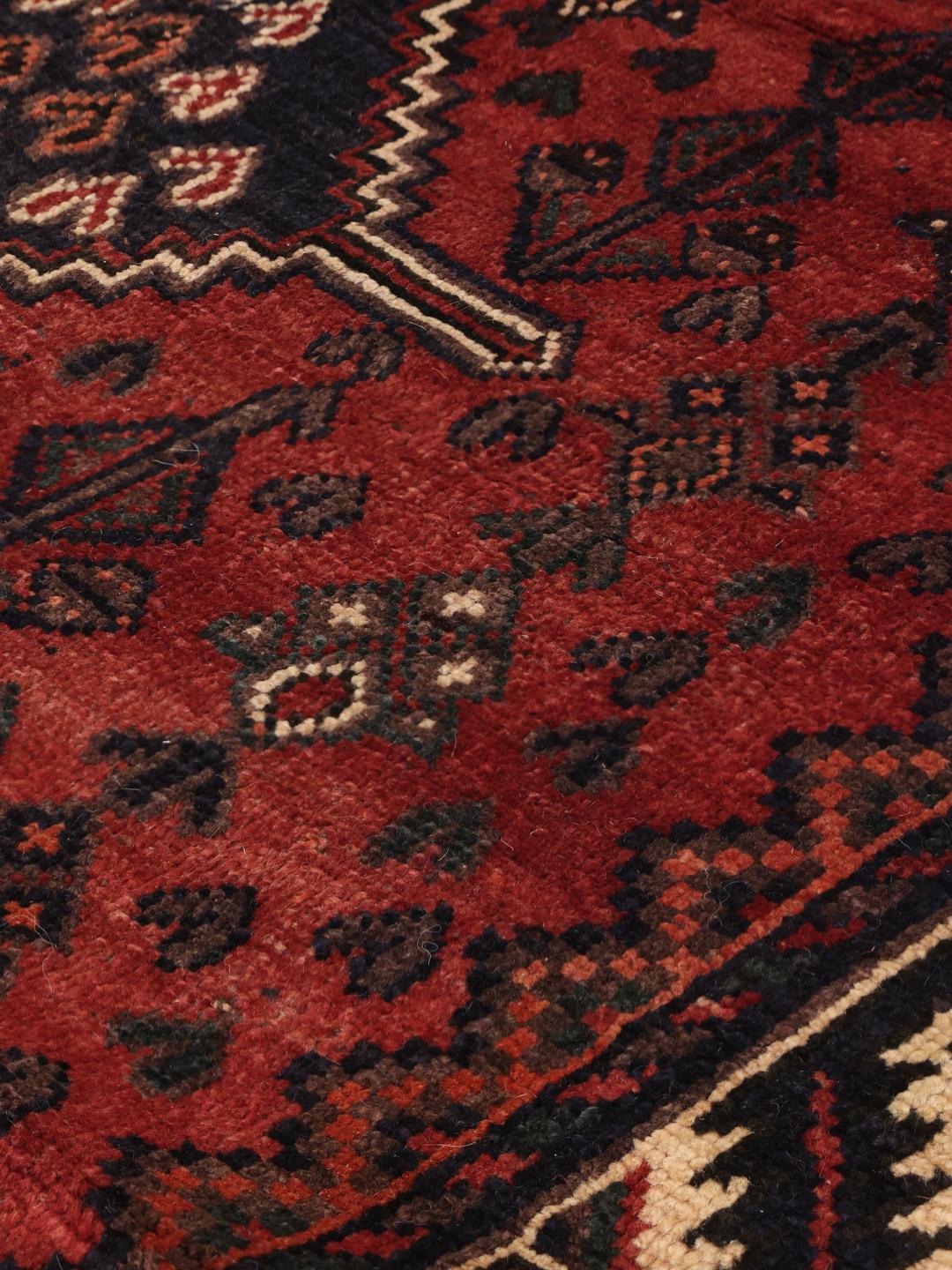 A hand-knotted Shiraz rug from the Middle East featuring geometric patterns in dark red and deep blue