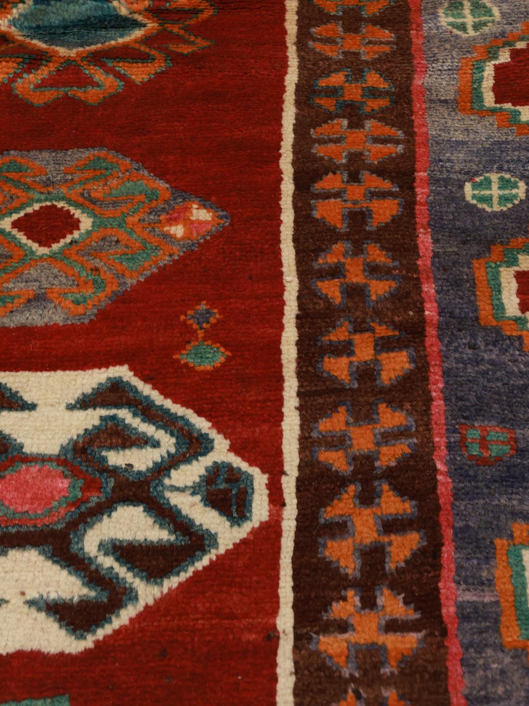 A hand-knotted Ghashghai rug from the Middle East with a vibrant red field and geometric patterns.