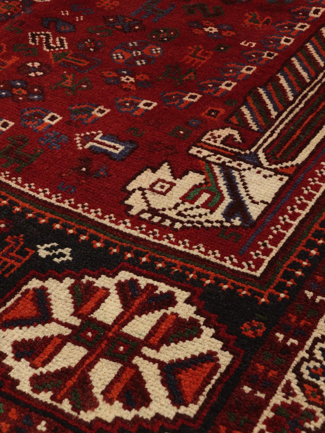 A red hand-knotted wool rug with geometric tribal patterns from the Middle East.