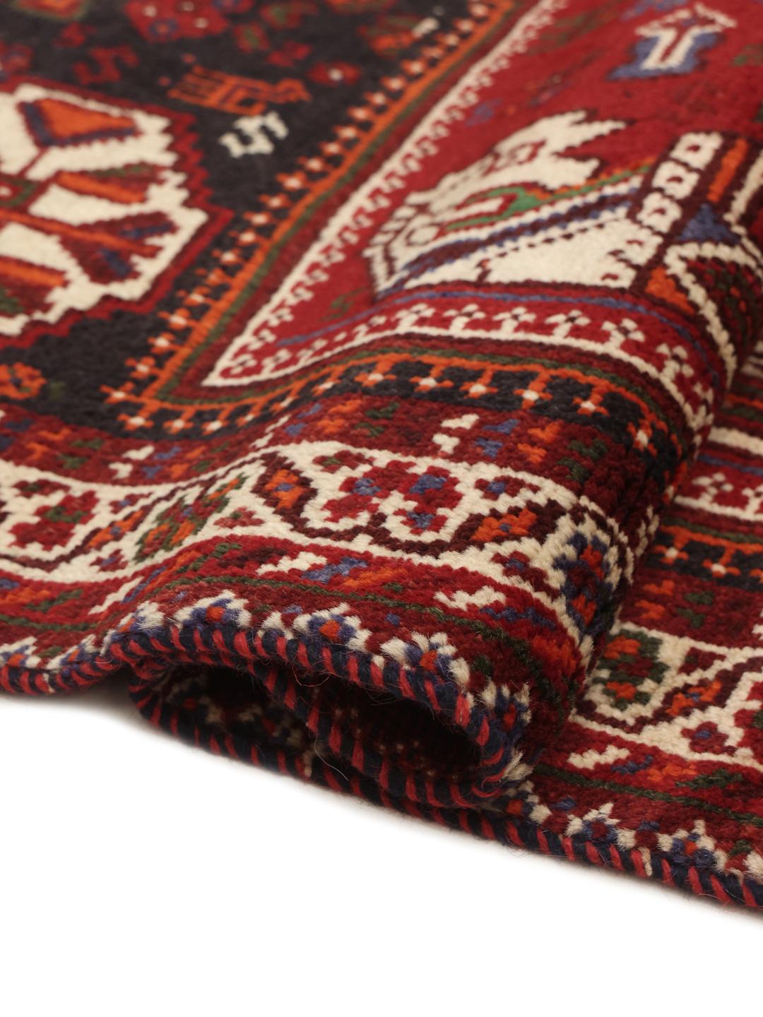 A red hand-knotted wool rug with geometric tribal patterns from the Middle East.