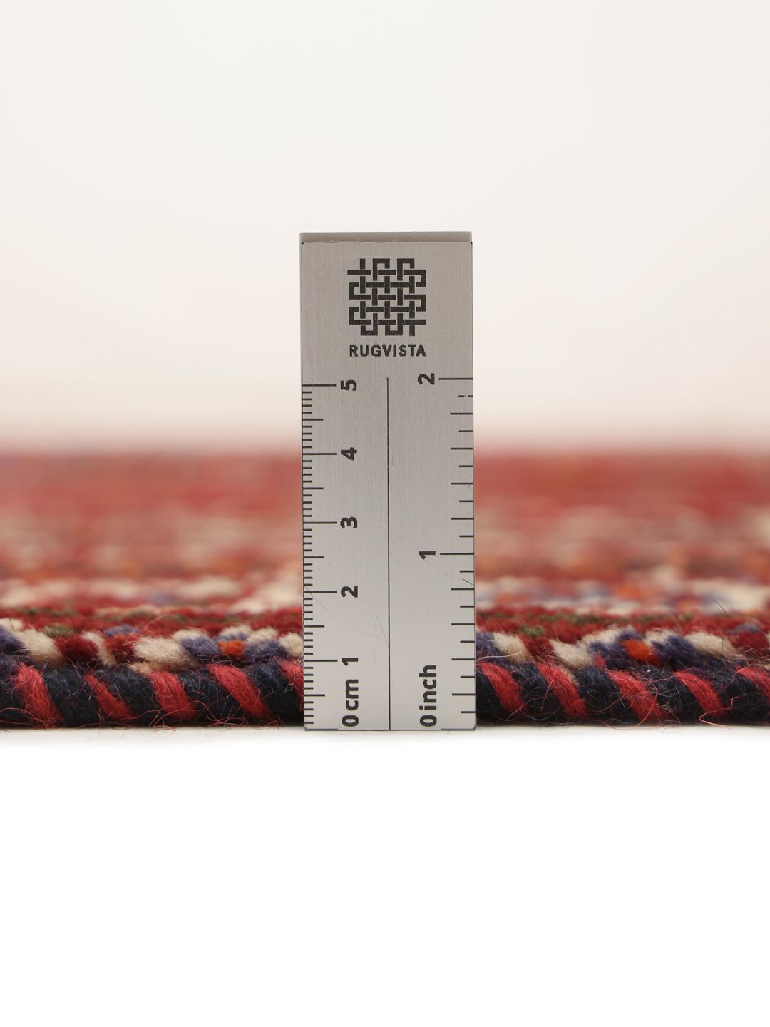 A red hand-knotted wool rug with geometric tribal patterns from the Middle East.